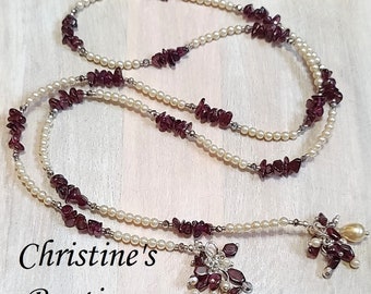 May include: A long, layered necklace with a pendant made of small, faceted, dark purple stones and white pearls. The necklace is made of two strands of white pearls and dark purple stones.