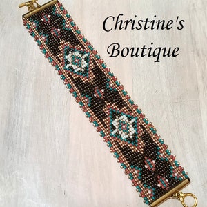 Op de afbeelding: Een kralenarmband met een geometrisch patroon in zwart, wit, turquoise en koperkleuren. De armband heeft goudkleurige sluitingen.