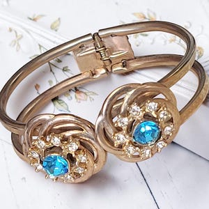May include: Vintage gold-tone hinged bracelet. The bracelet features two decorative circular elements with a central blue gemstone surrounded by clear crystals. The bracelet is designed with a clasp closure.