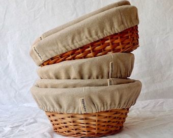 May include: Three beige linen-lined wicker bread baskets stacked on top of each other. The baskets are labeled "mainbäckerei" in black text.