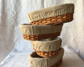 Puede incluir: Cuatro cestas de mimbre tejidas con forros de tela beige. Las cestas están apiladas una encima de la otra. Los forros tienen la palabra "marighella" impresa.