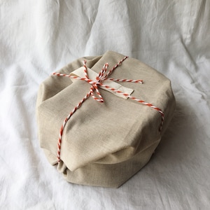 May include: A beige fabric gift box tied with red and white twine. The box is wrapped in a simple, rustic style.