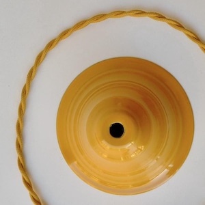 May include: A close-up of a yellow ochre-colored ceiling light fixture with a matching twisted cord. The fixture has a central hole and a circular design. The word "ochre" is in the top left corner.