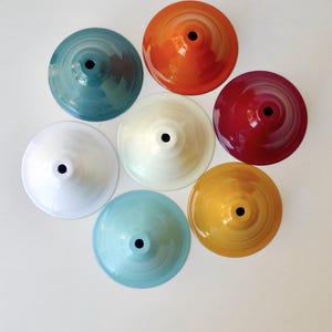 May include: A collection of eight colorful, cone-shaped objects arranged in a circular pattern. The objects are in shades of teal, orange, red, yellow, white, and light blue. Each has a central hole and a glossy finish, suggesting they are decorative or functional items.