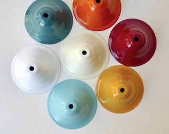 May include: A collection of seven circular, cone-shaped metal ceiling light canopy covers in various glossy colors including orange, teal, white, cream, red, light blue, and yellow, each featuring a small centered hole for a light fixture cord.