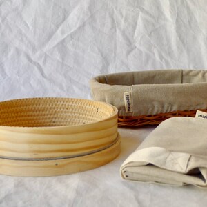 May include: A set of three beige linen bread baskets. The baskets are made of woven wicker and have a natural wood finish. The baskets are labeled "marjamolla".