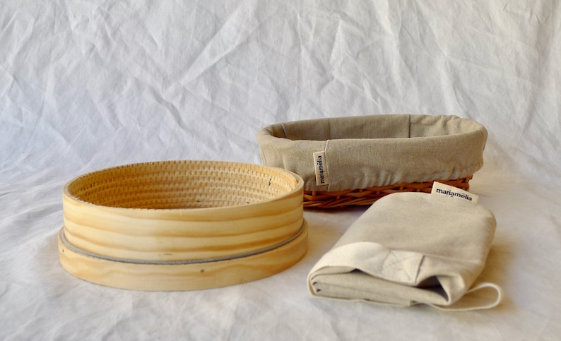 May include: A set of three beige linen bread baskets. The baskets are made of woven wicker and have a natural wood finish. The baskets are labeled "marjamolla".