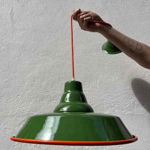 May include: A glossy dark green pendant lamp with a wide, flared shade and a smooth finish. The lamp features a bright orange cord and a matching orange trim along the bottom edge of the shade. The text "orange cord" is visible at the top.