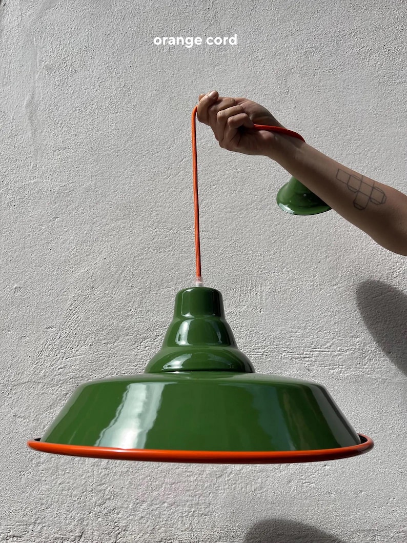 May include: A glossy dark green pendant lamp with a wide, flared shade and a smooth finish. The lamp features a bright orange cord and a matching orange trim along the bottom edge of the shade. The text "orange cord" is visible at the top.