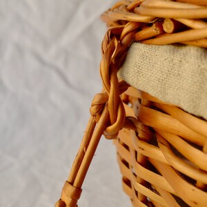 Pode incluir: Um close-up de uma cesta de vime tecida com um forro de linho natural. A cesta tem uma al&ccedil;a feita de vime tecido.