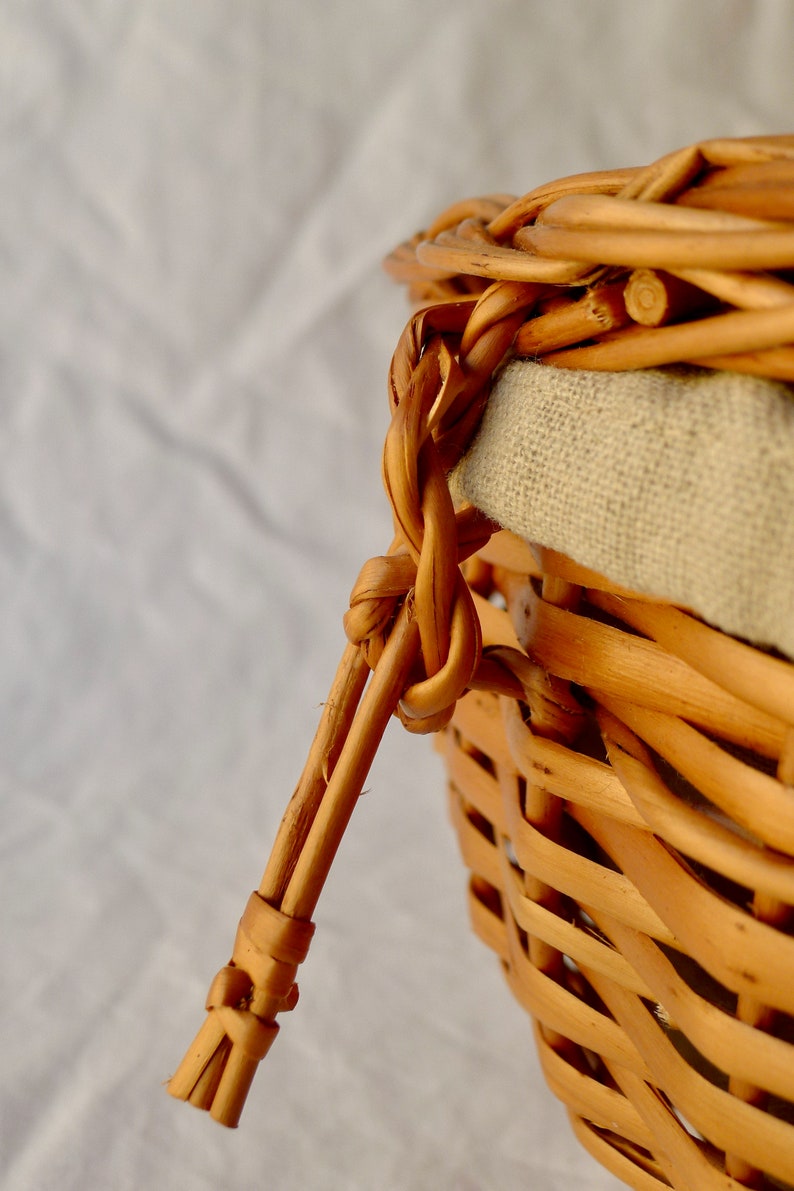 Pode incluir: Um close-up de uma cesta de vime tecida com um forro de linho natural. A cesta tem uma al&ccedil;a feita de vime tecido.