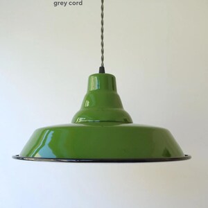 May include: A glossy green pendant light fixture with a wide, flared shade and a smooth, rounded top section. The lamp is suspended by a twisted grey cord. The bottom edge of the shade features a thin, dark rim, and the text grey cord is visible.