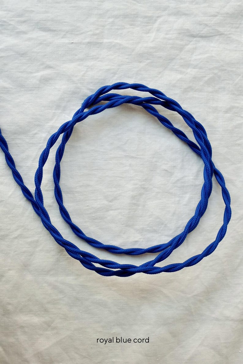 May include: A royal blue fabric-covered electrical cord featuring a twisted design. The cord is coiled into a circular shape and includes the text royal blue cord printed at the bottom of the image, indicating the color and type of the item.