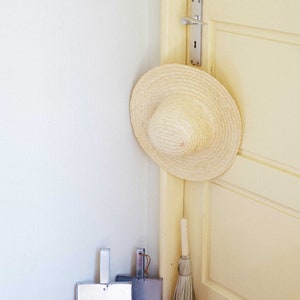 A straw hat hangs on a beige door's doorknob