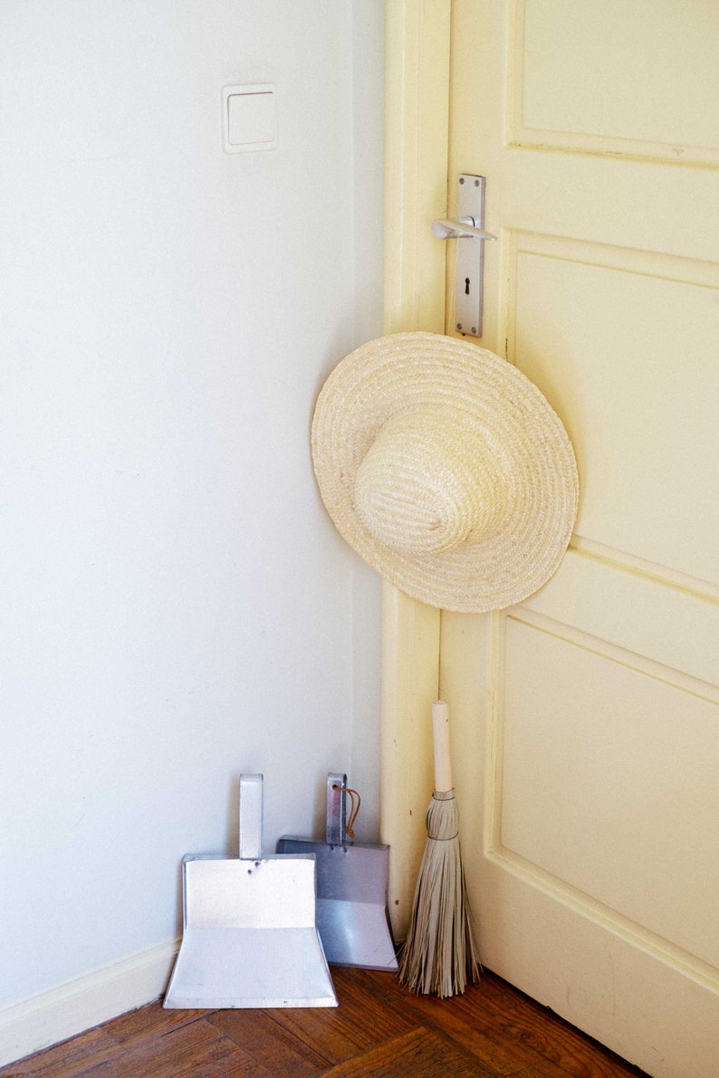 A straw hat hangs on a beige door's doorknob