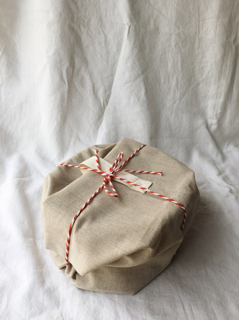 May include: A beige fabric gift box tied with red and white twine. The box is wrapped in a simple, rustic style.