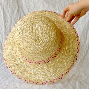 Puede incluir: Un sombrero de paja con ribete rosa. El sombrero est&aacute; tejido y tiene un ala ancha.