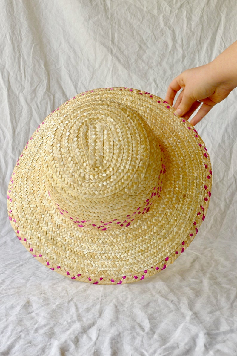 Puede incluir: Un sombrero de paja con ribete rosa. El sombrero est&aacute; tejido y tiene un ala ancha.
