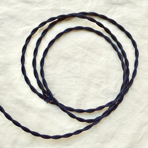 May include: A navy blue fabric-covered electrical cord featuring a twisted design. The cord is coiled into a circular shape, showcasing the textured, braided surface of the material. The text "navy blue cord" is printed at the bottom of the image.