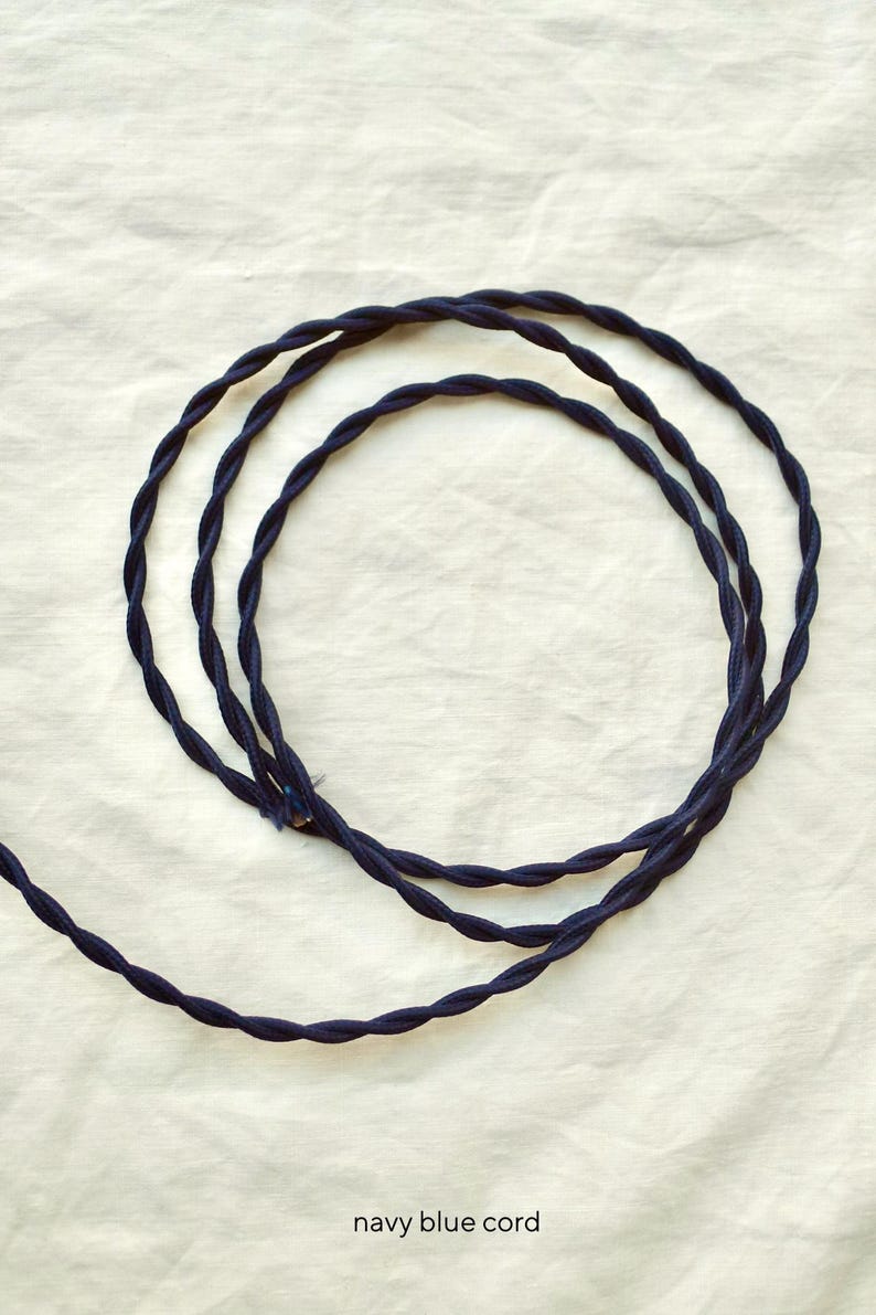 May include: A navy blue fabric-covered electrical cord featuring a twisted design. The cord is coiled into a circular shape, showcasing the textured, braided surface of the material. The text "navy blue cord" is printed at the bottom of the image.