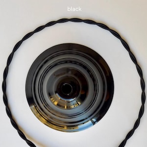 May include: A black circular ceiling canopy with a glossy finish and a central opening, surrounded by a length of black twisted fabric-covered electrical cord. The word black is printed in small white text at the top of the image.