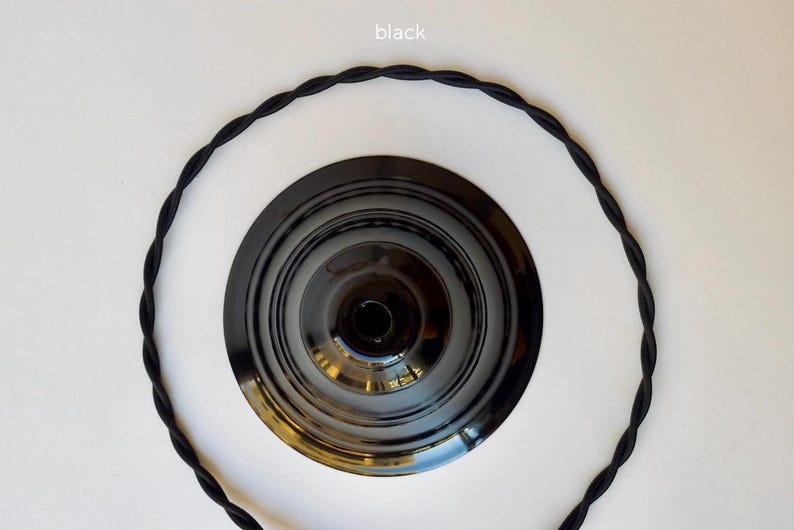 May include: A black circular ceiling canopy with a glossy finish and a central opening, surrounded by a length of black twisted fabric-covered electrical cord. The word black is printed in small white text at the top of the image.