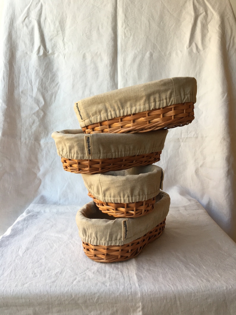 May include: Four woven wicker baskets with beige fabric liners. The baskets are stacked on top of each other. The liners have the word "marighella" printed on them.