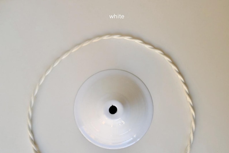 May include: A white ceiling canopy with a central circular opening, accompanied by a matching white twisted fabric electrical cord arranged in a circular shape. The word white is printed in small text above the canopy component.