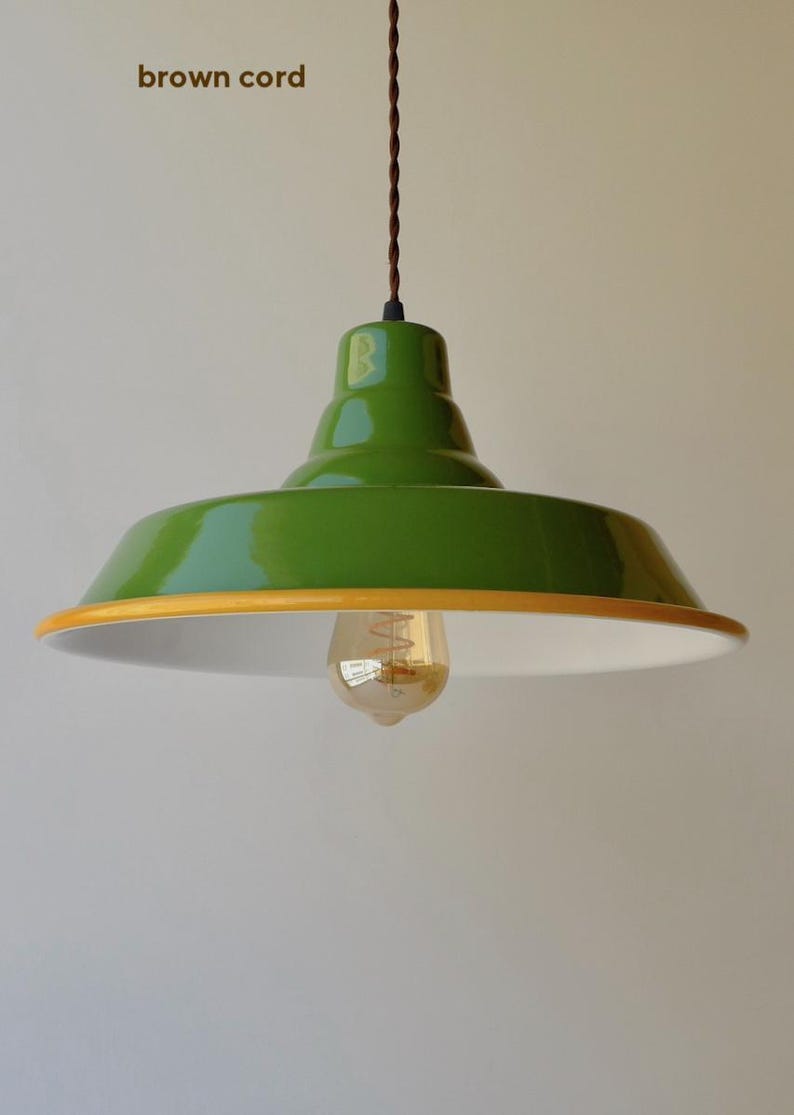 May include: A green pendant light with a glossy finish, a yellow rim, and a white interior. The fixture hangs from a brown cord and includes a single exposed Edison-style light bulb. The text brown cord is visible in the upper left corner.