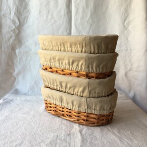 May include: Four oval wicker baskets with beige linen liners stacked on top of each other.