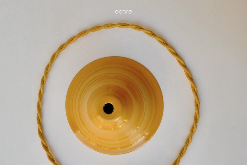 May include: A close-up of a yellow ochre-colored ceiling light fixture with a matching twisted cord. The fixture has a central hole and a circular design. The word "ochre" is in the top left corner.