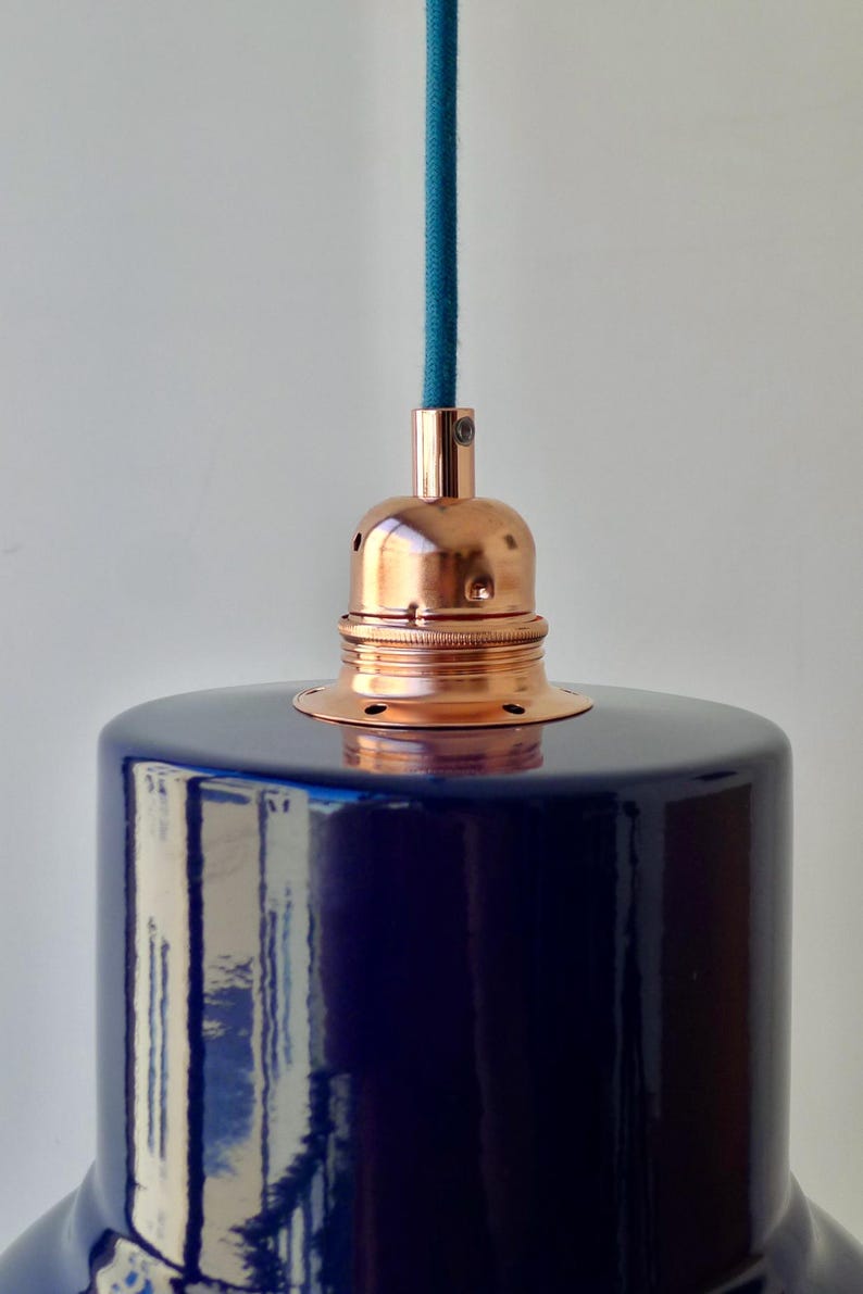 May include: A pendant light fixture featuring a glossy, deep navy blue cylindrical shade. The top of the shade is fitted with a polished copper metal socket holder, which connects to a textured teal blue fabric cord extending upward.