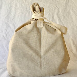 May include: A large, off-white canvas tote bag with a gathered top and a single strap. The bag is made of a natural, unbleached fabric.
