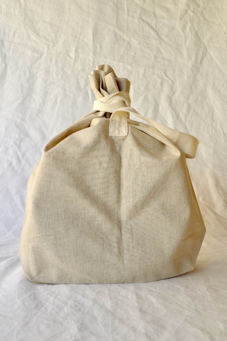 May include: A large, off-white canvas tote bag with a gathered top and a single strap. The bag is made of a natural, unbleached fabric.