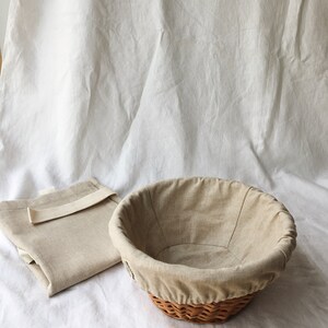 May include: A beige linen-lined wicker bread basket with a matching beige linen cloth on a white surface.