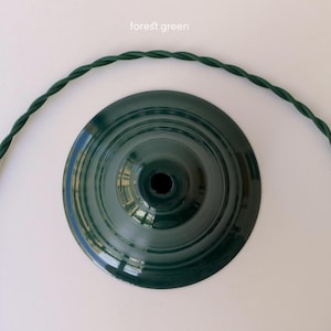May include: A forest green circular lamp shade base with a central opening, accompanied by a matching forest green twisted fabric electrical cord that curves around the base. The text "forest green" is printed above the lamp shade component.