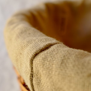 Pode incluir: Um close-up de uma cesta tecida com um forro de juta marrom. A cesta &eacute; feita de madeira natural e tem um visual r&uacute;stico.