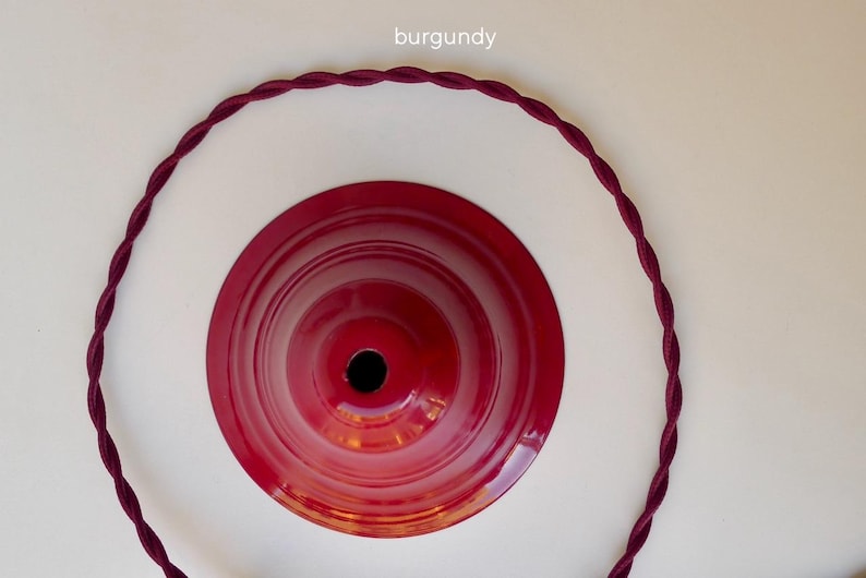 May include: A glossy burgundy metal ceiling canopy with a central circular opening, accompanied by a matching burgundy twisted fabric electrical cord arranged in a large circle around the canopy. The text burgundy is visible above.