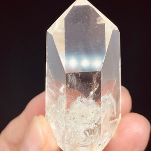 May include: A clear quartz crystal point with a double terminated point. The crystal has a natural, cloudy appearance with inclusions.