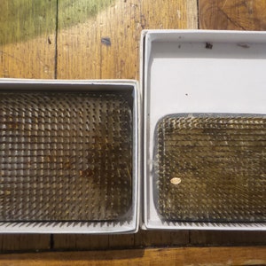 Op de afbeelding: Twee witte dozen met deksels die een set van twee naaldborden bevatten. De naaldborden zijn gemaakt van metaal en hebben een raster van scherpe naalden. Het grotere naaldbord bevindt zich in de linker doos en het kleinere naaldbord in de rechter doos.