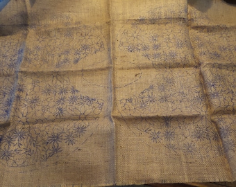 Könnte beinhalten: Ein brauner Jutestoff mit einem blauen Blumenmuster darauf gedruckt. Der Stoff ist in der Mitte gefaltet und das Muster ist auf beiden Seiten sichtbar.