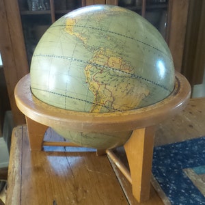 May include: A vintage wooden globe with a green and yellow map of the world. The globe is on a wooden stand with three legs.