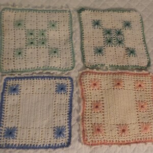 Puede incluir: Cuatro cuadrados de ganchillo hechos a mano en blanco, con diferentes bordados florales de colores. Los cuadrados tienen un borde festoneado en verde, azul y melocotón. Los cuadrados están dispuestos en forma cuadrada.