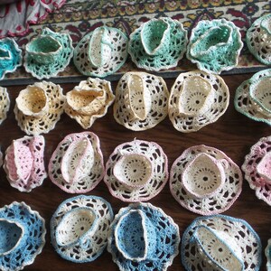 May include: A collection of 20 crocheted doilies in various colors, including pink, blue, white, and yellow. The doilies are arranged in rows on a wooden surface.