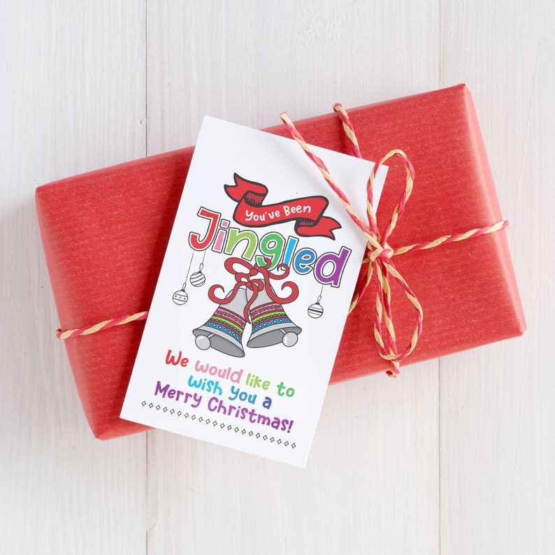 May include: A white gift tag with a colorful illustration of two bells and the text "You've Been Jingle-d". The tag also includes the text "We would like to wish you a Merry Christmas!"