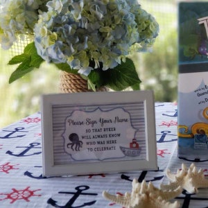 May include: White sign with blue and gray stripes, featuring an octopus and a red boat. The sign reads "Please Sign Your Name So That Ryker Will Always Know Who Was Here To Celebrate".