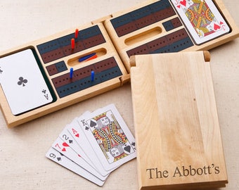 May include: A wooden cribbage board game set with a personalized inscription "The Abbott's". The board folds in half and includes a deck of cards and pegs.