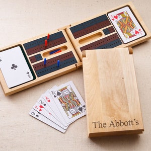 May include: A wooden cribbage board game set with a personalized inscription "The Abbott's". The board folds in half and includes a deck of cards and pegs.