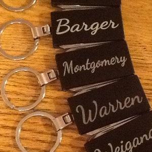 May include: Five black leather keychains with silver metal rings. Each keychain has a different name engraved in silver lettering: McNabb, Barger, Montgomery, Warren, and Weigand.