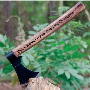 May include: A black-handled axe with a wooden handle engraved with the text "Devin Keener - Axe Throwing Champion".